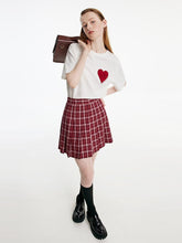 A lady wears a T-shirt and a plaid skirt.